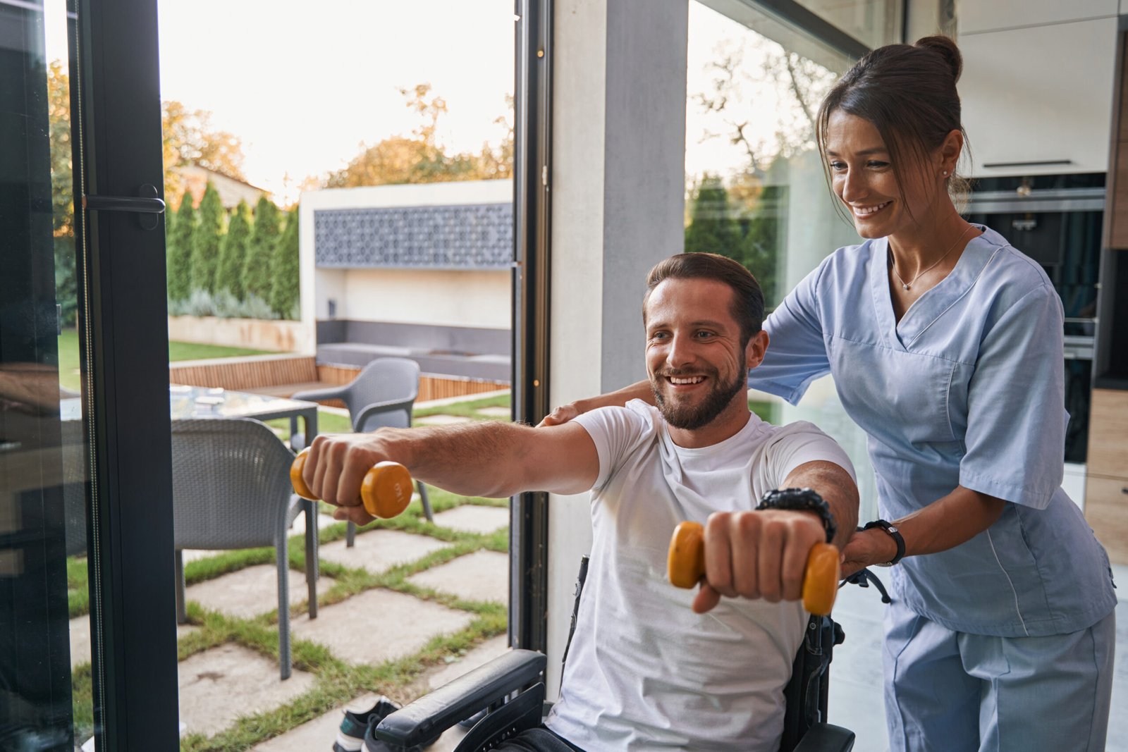 Positive male patient doing rehabilitation exercises with female physiotherapist in the room indoors